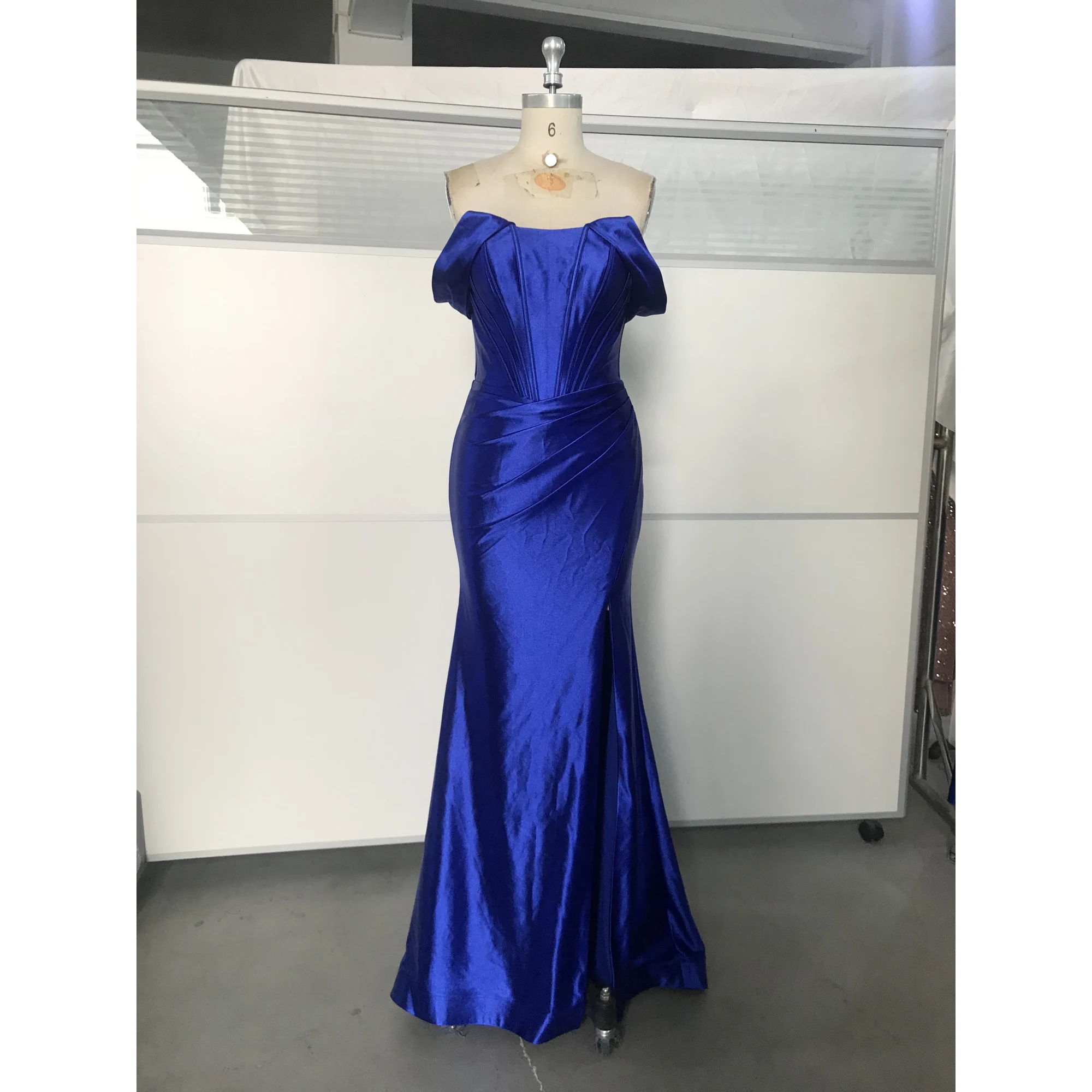 Stunning Royal Blue Stretch Satin off-the-shoulder mermaid gown with structured corset bodice, pleated details, and high slit on a dress form, showcasing luxurious sheen and elegant silhouette.