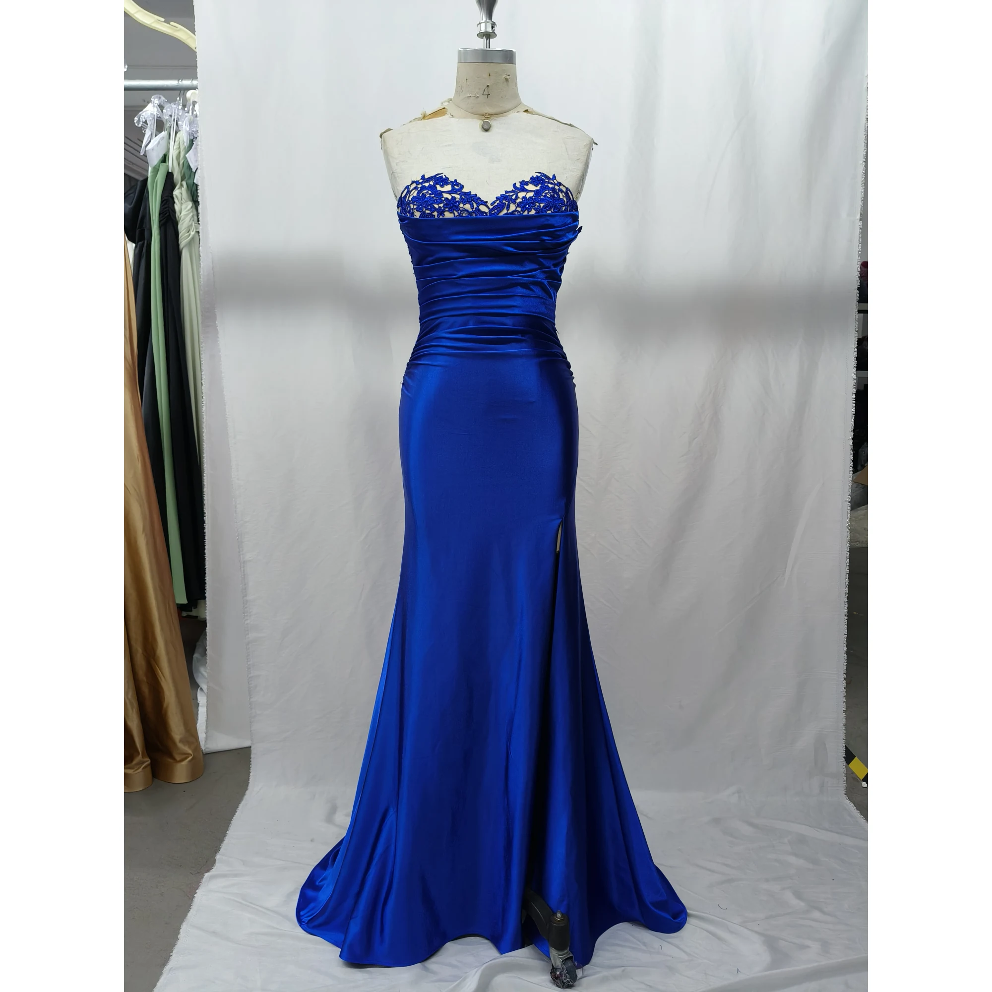 Stunning royal blue stretch satin mermaid gown featuring a strapless sweetheart neckline adorned with intricate rhinestone-embellished blue lace appliques, ruched bodice, and a figure-hugging silhouette with a side slit.