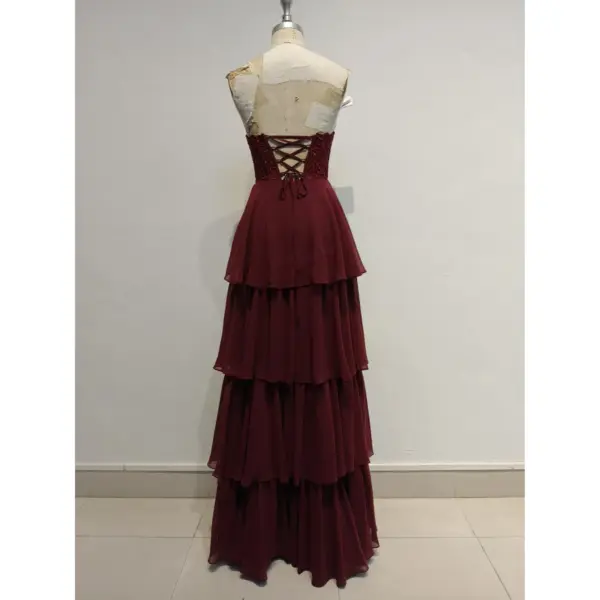 Back view of the Elizabeth Burgundy tiered chiffon ball gown showcasing the elegant lace-up corset back with delicate lace and rhinestone details, flowing into a multi-tiered chiffon skirt.