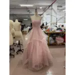 Front view of the Ophelia baby pink sparkle tulle ball gown featuring a sweetheart neckline with intricate floral applique embroidery, hand-beaded bodice, spaghetti straps and a dramatic multi-tiered ruffled skirt with scattered glitter details on a mannequin in a workshop setting.