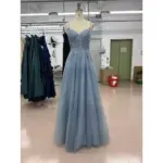 Front view of the Iris Sparkle Tulle Embroidered A-Line Gown in dusty blue featuring a sweetheart neckline with intricate floral embroidery, beaded lace appliqués, and sparkling tulle skirt with delicate sequin details on a dress form in a workshop setting.