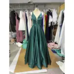 Stunning Clelia in rich Forest green Polyester Satin, featuring a plunging V-neckline, fitted bodice, and dramatic full ball gown skirt with natural volume and luxurious sheen. The deep emerald tone and silky fabric create a show-stopping prom silhouette with practical side pockets.