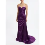 Model wearing the Laurence Eggplant Stretch Satin Ruched Mermaid Gown featuring a strapless sweetheart neckline adorned with intricate beaded lace appliques, ruched bodice and hip detailing that creates a figure-flattering mermaid silhouette in rich purple stretch satin fabric with a dramatic sweeping train.