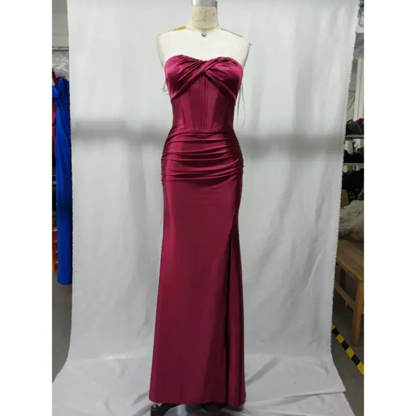 Stunning strapless sweetheart neckline Burgundy stretch satin mermaid gown by Alex featuring ruched bodice, internal boning, and dramatic high slit on a mannequin in a studio setting