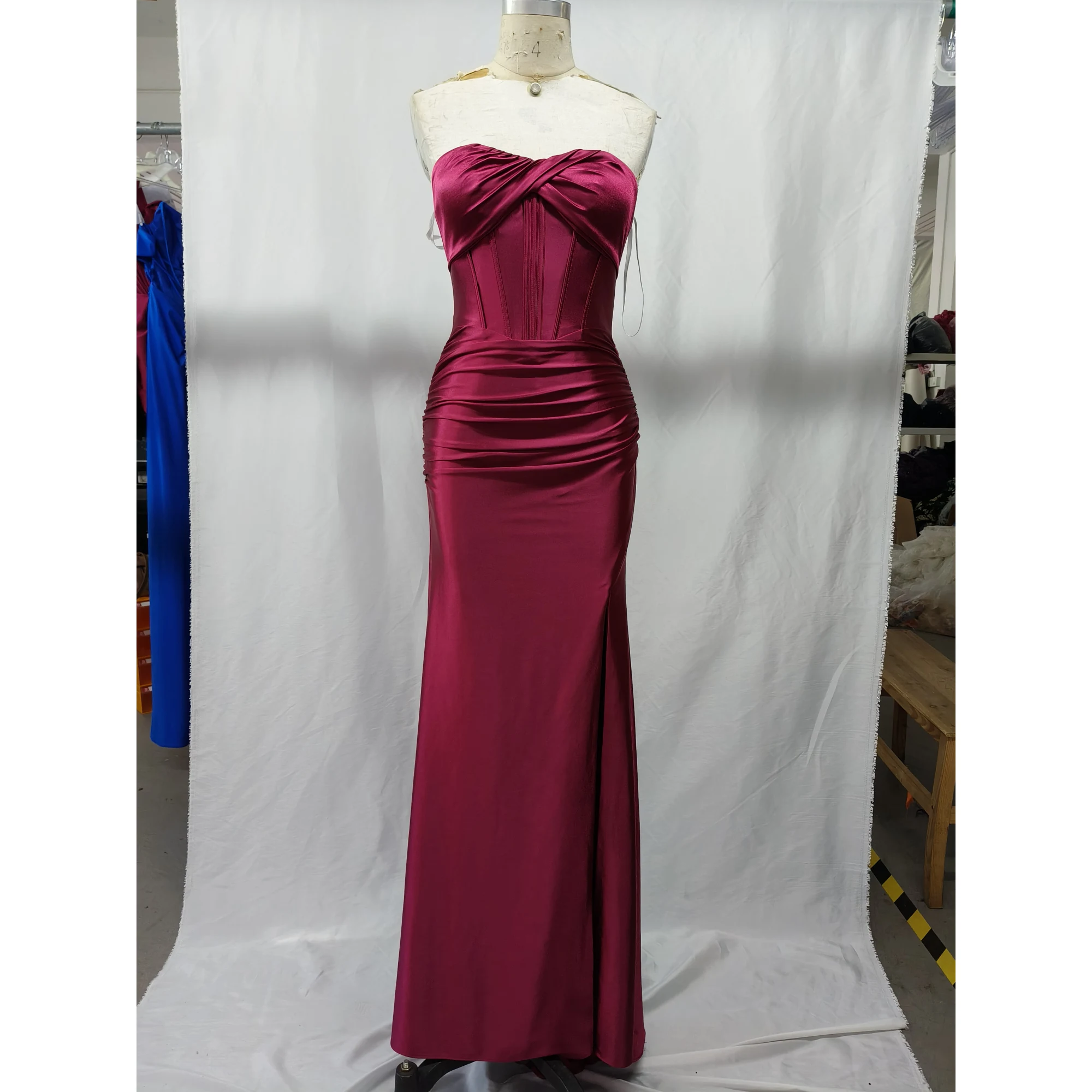 Stunning strapless sweetheart neckline Burgundy stretch satin mermaid gown by Alex featuring ruched bodice, internal boning, and dramatic high slit on a mannequin in a studio setting