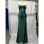 Stunning teal stretch satin mermaid gown on a mannequin, featuring a strapless sweetheart neckline with twisted ruched bodice, structured corset boning, a keyhole cutout, and a dramatic high slit that reveals the leg. The luxurious fabric drapes beautifully in rich teal.