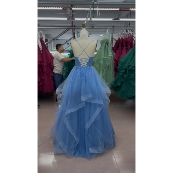 Back view of the Gianna Sky Blue tulle ball gown showcasing a criss-cross lace-up corset back with delicate blue straps, intricate lace appliqué detailing at the waist, and cascading layered ruffles in airy sky blue tulle.